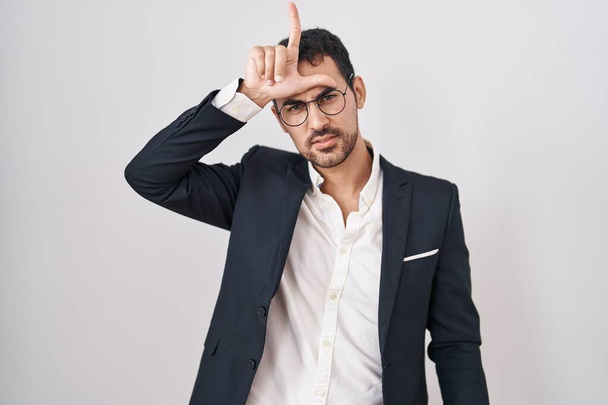 Handsome business hispanic man standing over white background making fun of people with fingers on forehead doing loser gesture mocking and insulting.  - Photo, Image