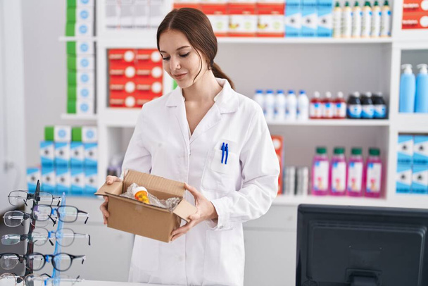 Νεαρή γυναίκα φαρμακοποιός κρατώντας συσκευασία με χάπια στο φαρμακείο - Φωτογραφία, εικόνα