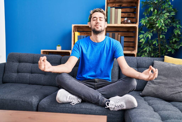 Young man doing yoga exercise sitting on sofa at home - Photo, Image