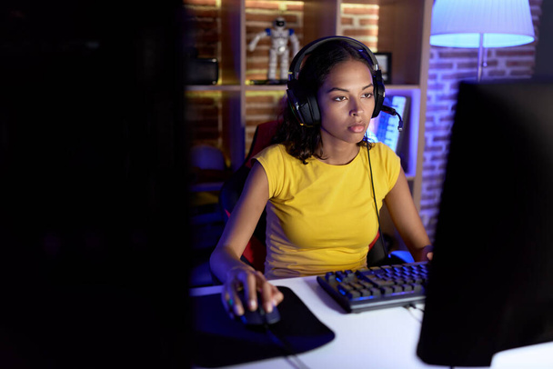 Young african american woman streamer playing video game using computer at gaming room - Valokuva, kuva