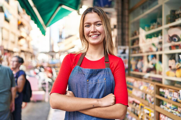 Young hispanic woman shop assistant standing with arms crossed gesture at street - Photo, Image