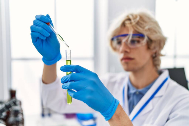 Young blond man scientist pouring liquid on test tube at laboratory - Photo, Image
