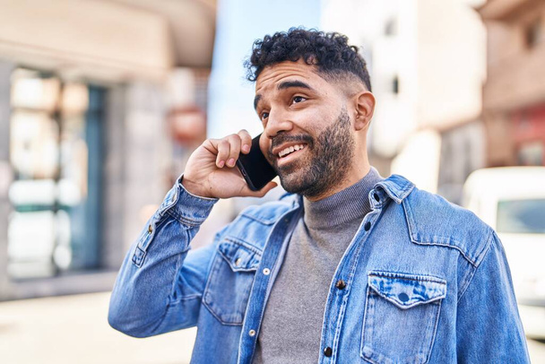 Jeune homme hispanique souriant confiant parler sur le smartphone à la rue - Photo, image