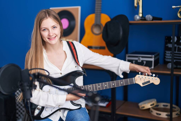 Jovem artista caucasiana sorrindo confiante tocando guitarra elétrica no estúdio de música - Foto, Imagem
