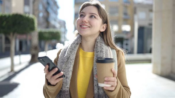 若いですブロンド女性使用スマートフォン飲料コーヒーでストリート - 写真・画像