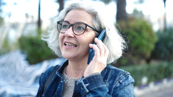 Mujer de mediana edad con el pelo gris hablando por teléfono en el parque - Foto, Imagen