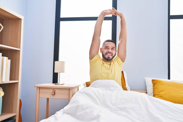 Genç latin adam yatak odasında kollarını esneterek uyanıyor. - Fotoğraf, Görsel