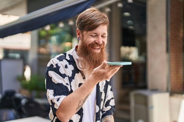 Fiatal vörös férfi mosolygós magabiztos beszél az okostelefonon az utcán - Fotó, kép