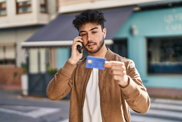 Молодий іспаномовний чоловік використовує смартфон і кредитну картку на вулиці
 - Фото, зображення