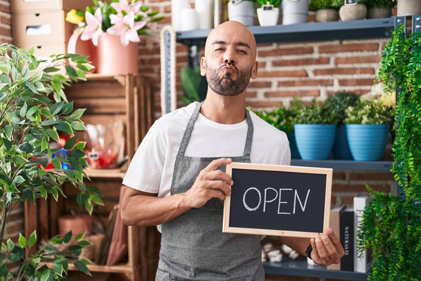 Middle age bald man working at florist holding open sign looking at the camera blowing a kiss being lovely and sexy. love expression.  - Photo, Image