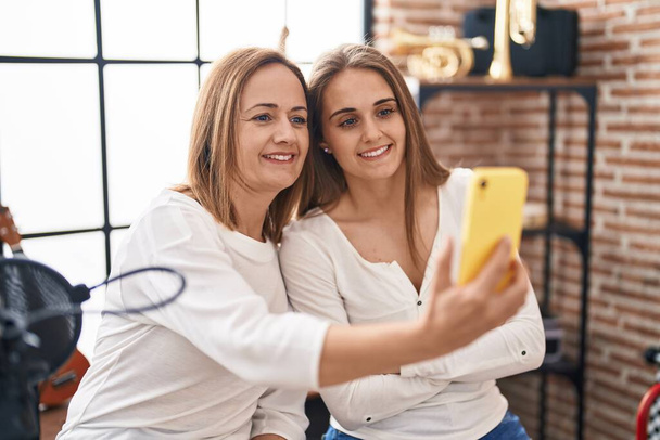 Δύο γυναίκες μουσικοί χαμογελώντας σίγουροι κάνουν selfie από το smartphone στο στούντιο μουσικής - Φωτογραφία, εικόνα