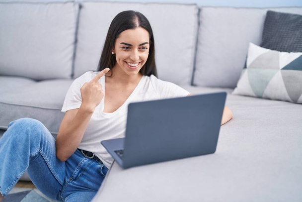 młoda brunetka kobieta za pomocą laptopa w domu uśmiechnięty szczęśliwy wskazując ręką i palcem  - Zdjęcie, obraz