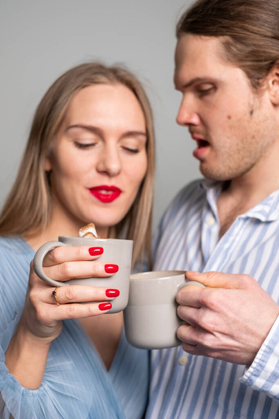 Surprised man and beautiful dreamy woman with red lips and nails and a ring on her finger. Young couple in light blue clothes drinking coffee. Copyspace - Photo, Image