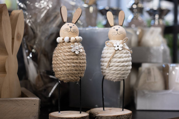 Lindos conejitos de Pascua sonrientes hechos de hilo de algodón con orejas y cabezas de madera sobre una base de madera en un estante. Conejo de Pascua de madera en una caja, materiales de decoración envueltos borrosos en el fondo. - Foto, imagen