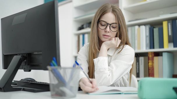 Junge blonde Studentin schreibt Computer auf Notizbuch im Hörsaal der Universität - Foto, Bild