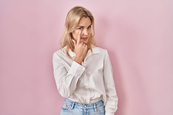 Young caucasian woman wearing casual white shirt over pink background pointing to the eye watching you gesture, suspicious expression  - Photo, Image