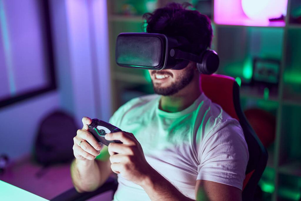 Joven streamer hispano usando gafas de realidad virtual jugando videojuego en sala gamin - Foto, imagen
