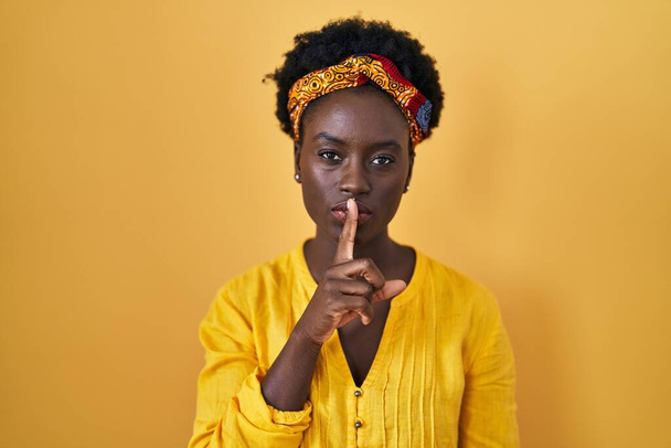 African young woman wearing african turban asking to be quiet with finger on lips. silence and secret concept.  - Φωτογραφία, εικόνα