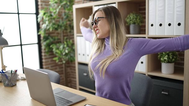 Młoda blondynka biznes pracownik za pomocą laptopa wyciągając ramiona w biurze - Zdjęcie, obraz
