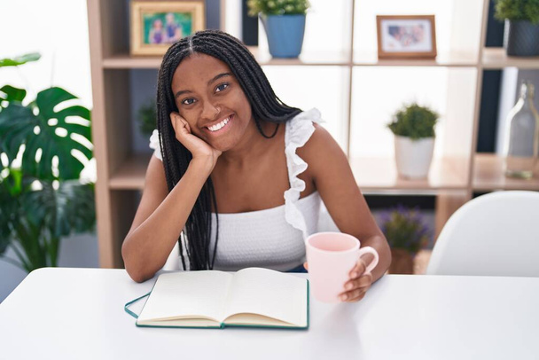 African american woman drinking coffee reading book at home - Photo, Image