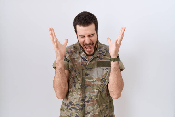 Joven hombre hispano vistiendo uniforme camuflaje del ejército celebrando loco y loco por el éxito con los brazos levantados y los ojos cerrados gritando emocionado. concepto ganador  - Foto, Imagen
