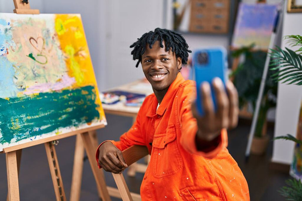 Afrikaanse amerikaanse man kunstenaar glimlachen zelfverzekerd maken selfie door smartphone in kunststudio - Foto, afbeelding