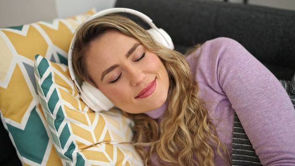 Junge blonde Frau hört zu Hause entspannt Musik auf dem Sofa - Foto, Bild