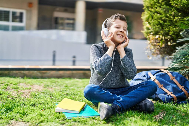 Rubio niño estudiante sonriendo confiado escuchando música en el parque - Foto, Imagen