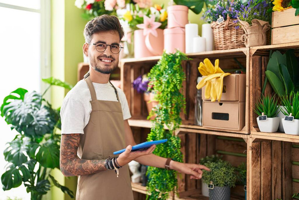 Joven florista hispano sonriendo confiado usando touchpad en floristería - Foto, Imagen