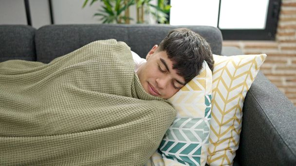 De jonge Spaanse man ligt thuis op de bank te slapen. - Foto, afbeelding