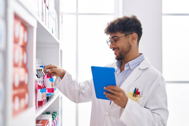 Молодий арабський чоловік фармацевт, використовуючи тачпад, тримає пляшку ліків в аптеці
 - Фото, зображення