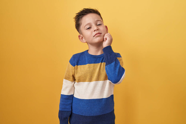 Pieni latino poika seisoo keltainen tausta ajattelu keskittyi epäilystä sormella leuka ja etsii ylös ihmetellen  - Valokuva, kuva