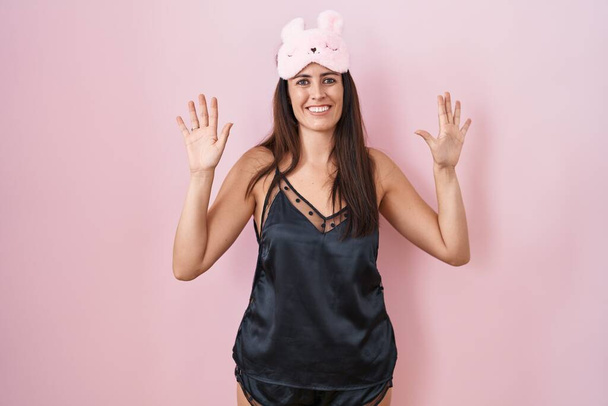 Young brunette woman wearing sleep mask and pyjama showing and pointing up with fingers number ten while smiling confident and happy.  - Fotografie, Obrázek