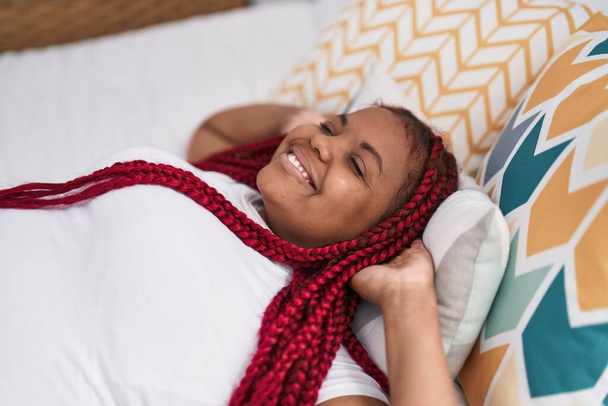 Afroamerykanka uśmiecha się pewnie zrelaksowany na łóżku w sypialni - Zdjęcie, obraz