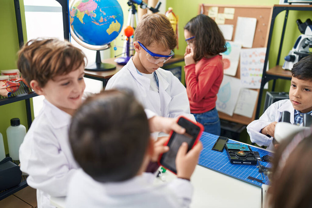 研究室の教室でスマホを修復する顕微鏡を使っている子供たちのグループ - 写真・画像