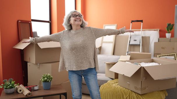 Frau mittleren Alters mit grauen Haaren lächelt selbstbewusst und steht mit offenen Armen im neuen Zuhause - Foto, Bild