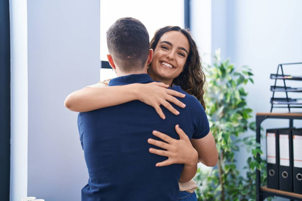 Young hispanic couple business workers hugging each other standing at office - Фото, изображение