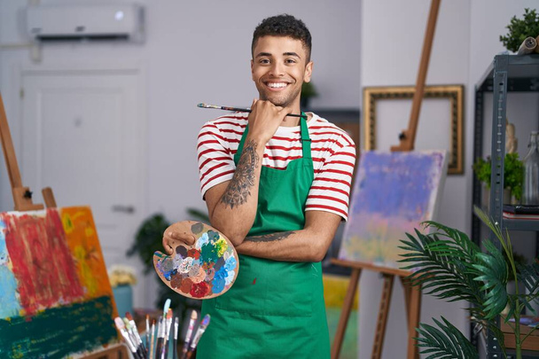 Бразильський молодий чоловік, який тримає палітру художника на художній студії, посміхається з щасливою і прохолодною посмішкою на обличчі. з зубами.  - Фото, зображення