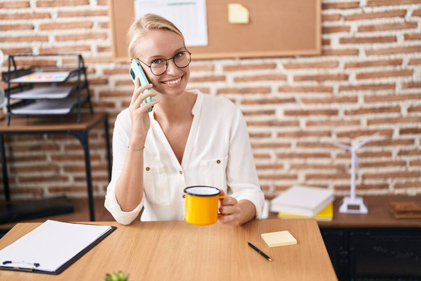 Jovem loira mulher empresária falando no smartphone bebendo café no escritório - Foto, Imagem