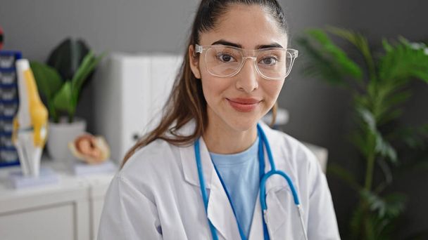 Young beautiful hispanic woman doctor smiling confident sitting on table at clinic - Foto, Imagen