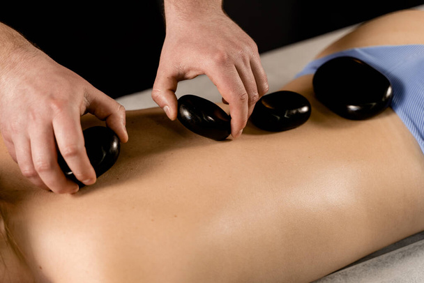 Masseur placed hot stone on the back of woman. Manual therapy in spa - Foto, afbeelding
