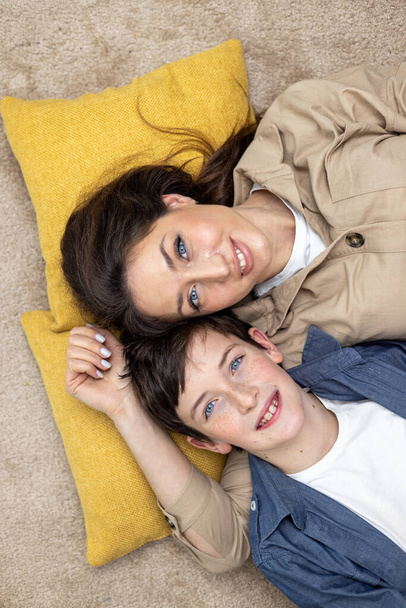 Portrait of a family, a mother and a teenage son lying on pillows, hugging, looking at the camera, smiling. Close-up photo, vertical photo, top photo. - Фото, зображення