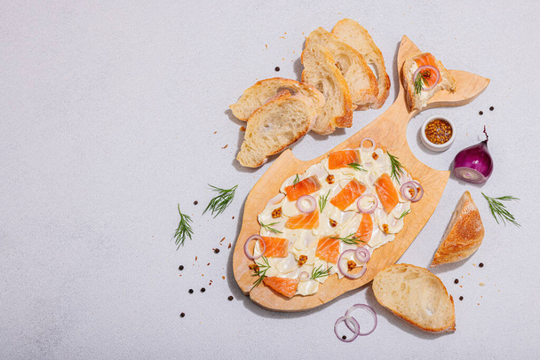 Trendy Butter Board with salmon, red onion, mustard and fresh dill. Homemade snack with baguette bread, healthy vegetarian concept for friend party. Light stone concrete background, top view - Photo, Image