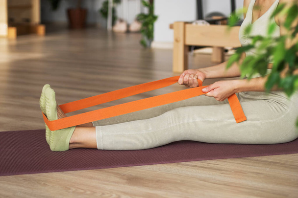 Trainer doing leg stretching exercises with orange fitness rubber bands. Fitness trainer doing exercises in pilates yoga studio. Concept of beauty, body care, health. Women health club.  - Fotoğraf, Görsel
