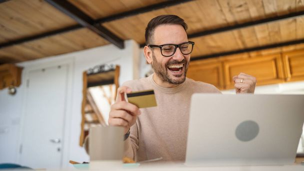 Ein Mann erwachsen reifen kaukasischen Mann sitzen zu Hause glücklich lächeln mit Laptop Computer halten Bank Kreditkarte Online-Shopping kaufen auf Internet-Konzept echte Menschen kopieren Raum E-Commerce E-Banking-Service - Foto, Bild