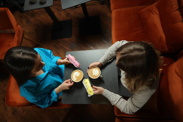 Young women with coffee and eclairs spending time together in cafe, above view - Photo, Image