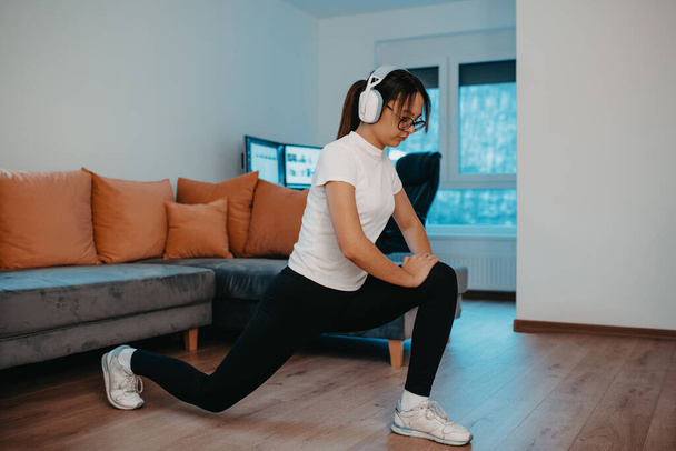 Egy nő nyújtózkodik a lakásában kora reggel edzés után, tükrözve elkötelezettségét az egészséges életmód iránt. Ez a pillanat rávilágít a rendszeres testmozgás és öngondoskodás fontosságára. - Fotó, kép