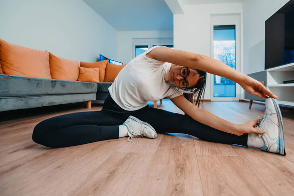 A woman stretching in her apartment during early morning after training , reflecting her dedication to a healthy lifestyle. This moment highlights the importance of regular exercise and self-care - 写真・画像