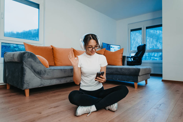 Una mujer haciendo ejercicio en casa con auriculares y smartphone para una videollamada. Refleja el estilo de vida moderno, la tecnología de mezcla, la salud y la conectividad para el bienestar holístico.  - Foto, imagen