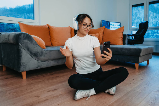 A woman doing home workout with headphones and smartphone for a video call. Reflects modern lifestyle, blending technology, health, and connectivity for holistic well-being.  - Photo, Image